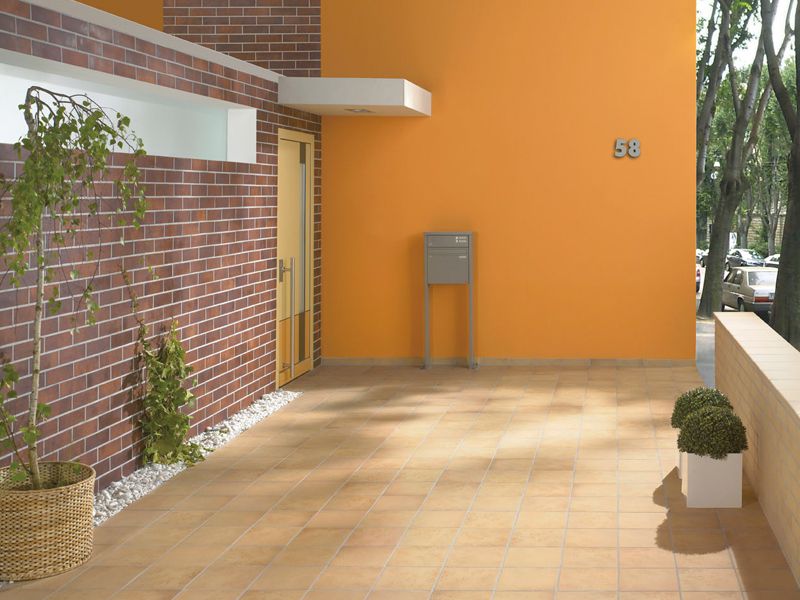 Moderner Eingangsbereich mit Granitfliesen, Hausnummer 58, Briefkasten, Pflanzen und gelb-oranger Wand.